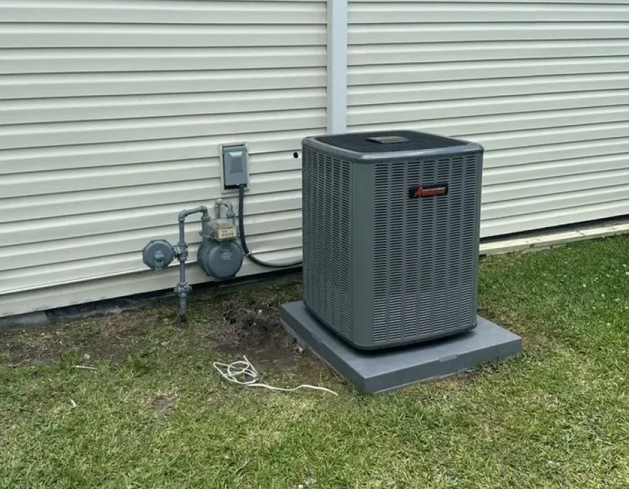 Amana outdoor AC condenser unit installed next to a residential siding wall.